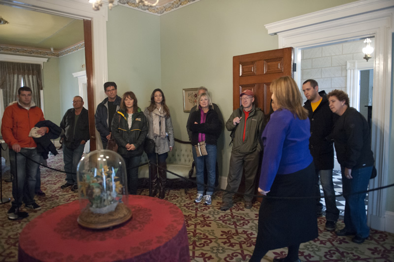 A DCASE Volunteer stands in the Clarke House Musuem living room with a group on a free public tour